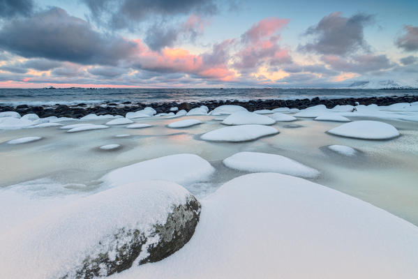 Dawn on the cold sea surrounded by snowy  rocks shaped by wind and ice at Eggum Vestvagøy Island Lofoten Islands Norway Europe