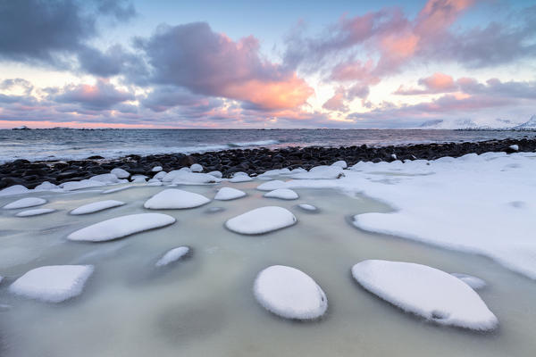 Dawn on the cold sea surrounded by snowy  rocks shaped by wind and ice at Eggum Vestvagøy Island Lofoten Islands Norway Europe