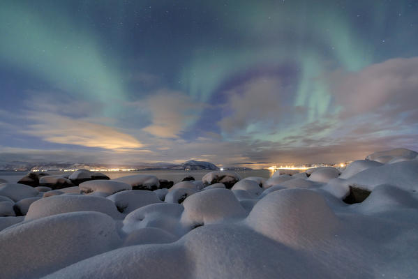 The pink light and the aurora borealis illuminate the snowy landscape on a starry night Strønstad Lofoten Islands Norway Europe