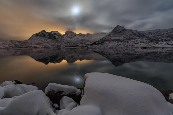 The light of the moon and the snowy peaks are reflected in the cold sea at Svolvaer Lofoten Islands Norway Europe