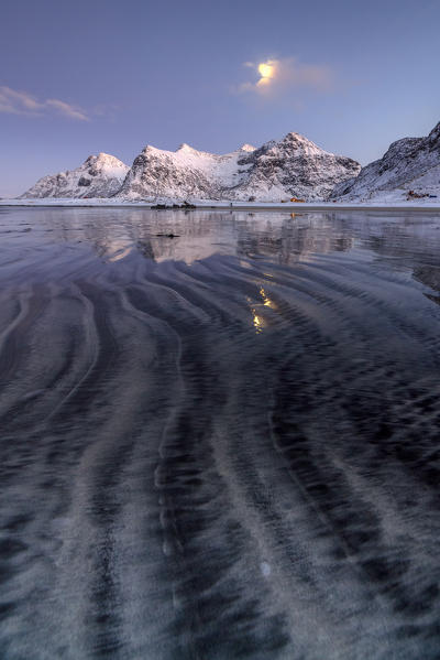 Waves and ice on the surreal Skagsanden beach surrounded by snowy peaks Flakstad Nordland county Lofoten Islands Norway Europe