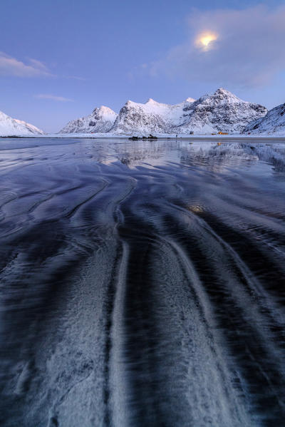 Waves and ice on the surreal Skagsanden beach surrounded by snowy peaks Flakstad Nordland county Lofoten Islands Norway Europe