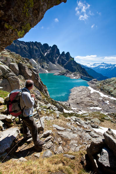 A hiker near the Carlo Emilio refuge looking the blue waters of Truzzo dam from above. Valchiavenna. Vallespluga. Valtellina. Lombardy. Italy. Europe