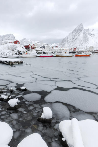 Icy sea and snowy peaks around the typical houses called rorbu and fishing boats Hamnøy Lofoten Islands Northern Norway Europe