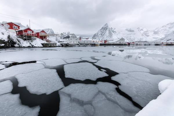 Icy sea and snowy peaks around the typical houses called rorbu and fishing boats Hamnøy Lofoten Islands Northern Norway Europe