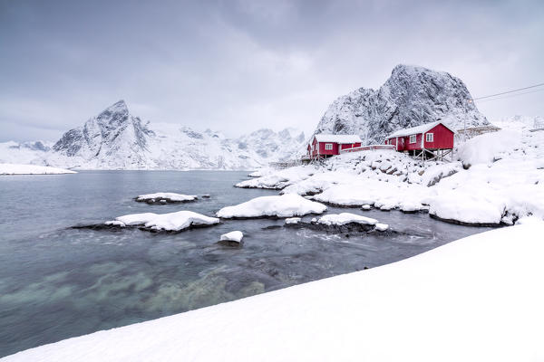 The snowy peaks and frozen sea frame the typical fisherman houses called Rorbu Hamnøy Lofoten Islands Northern Norway Europe