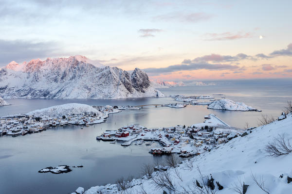 The pink colors of sunset and snowy peaks surround the fishing villages Reine Nordland Lofoten Islands Norway Europe