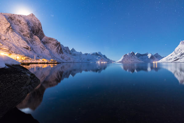 The snowy peaks are reflected in the frozen sea on a starry winter night Reine Bay Nordland Lofoten Islands Norway Europe