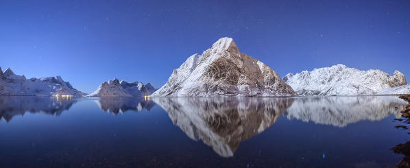 Panoramic view of snowy peaks reflected in the frozen sea on a starry night Reine Bay Nordland Lofoten Islands Norway Europe