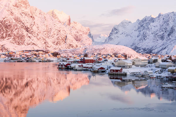 Pink sunrise and snowy peaks frame the  frozen sea and the fishing village Reine Bay Nordland Lofoten Islands Norway Europe