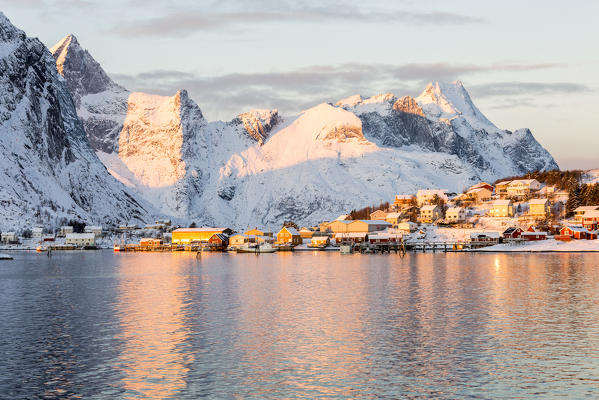 The pink colors of sunrise and snowy peaks are reflected in the cold sea Reine Bay Nordland Lofoten Islands Norway Europe