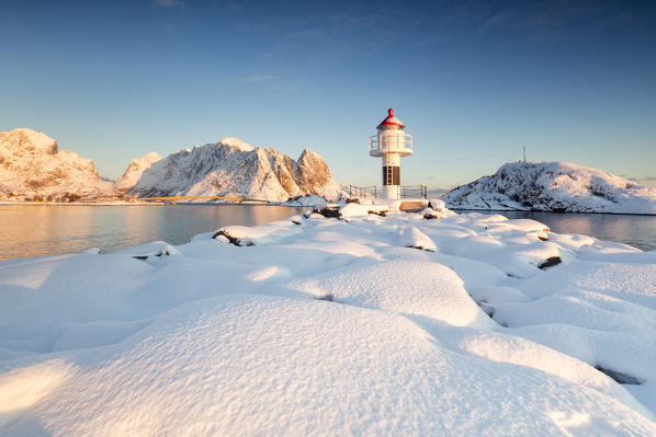 The lighthouse surrounded by snow frames the snowy peaks and the frozen sea Reine Nordland Lofoten Islands Norway Europe