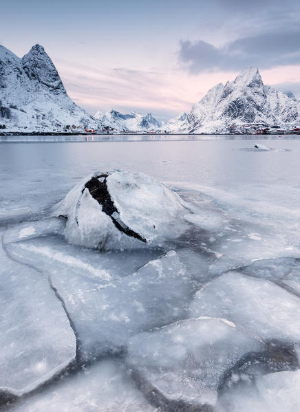 The frozen sea and the snowy peaks frame the fishing village at sunset Reine Nordland Lofoten Islands Norway Europe