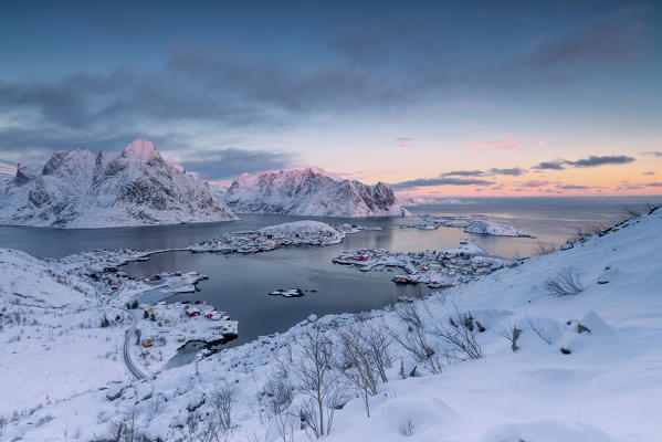 The pink colors of sunset and snowy peaks surround the fishing villages Reine Nordland Lofoten Islands Norway Europe