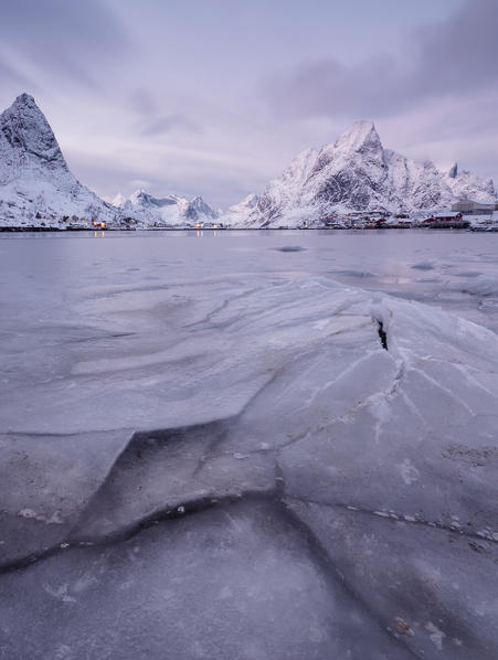 The frozen sea and the snowy peaks frame the fishing village at sunset Reine Nordland Lofoten Islands Norway Europe