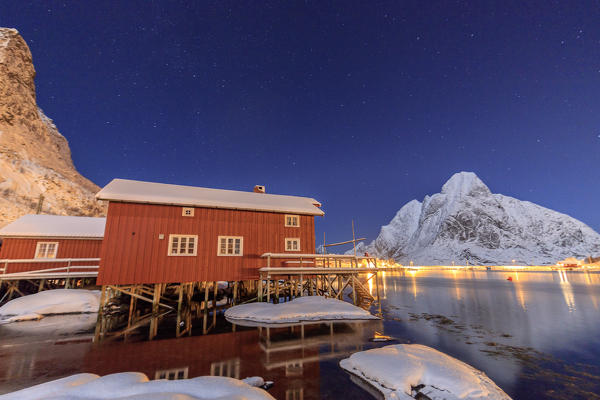 Starry night on the snowy peaks surrounded by the frozen sea and fishermen houses Reinevagen Bay Lofoten Islands Norway Europe