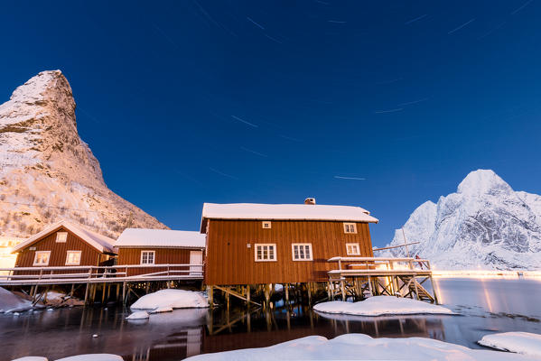 Starry night on the snowy peaks surrounded by the frozen sea and fishermen houses Reinevagen Bay Lofoten Islands Norway Europe