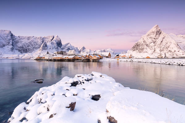 The colors of dawn frames the fishermen houses surrounded by snowy peaks Sakrisøy Reine Nordland Lofoten Islands Norway Europe