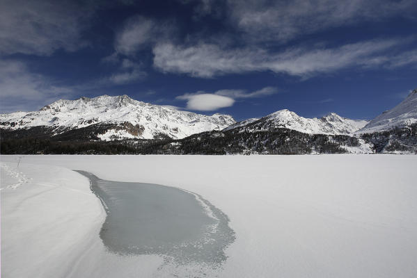 A strange shape of Water emerging from ice on the shores of the lake Sils in Engadine and in the background Piz Corvatsch Switzerland Europe