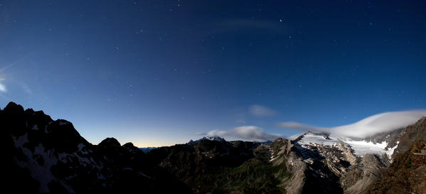 Looking the sky full of stars in a clear night from the refuge Martinelli, the clouds are moving on the glacier of Scerscen and in the distance you can also see Mount Disgrazia, Valmalenco, Lombardy Italy. Europe