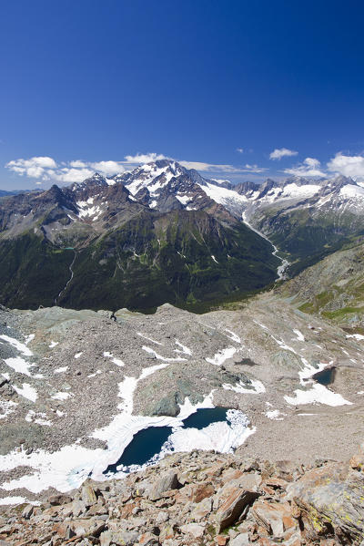 Overlooking Valmalenco and the small lakes Entova in the thaw season from the Forca dell'Entova. In the background Mount Disgrazia and the peaks of Chiareggio, Valmalenco, Valtellina, Lombardy Italy Europe