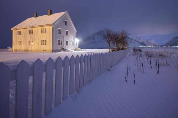 Lights on the typical wooden house surrounded by snow Flakstad Lofoten Islands Northern Norway Europe