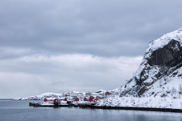 Cold sea and snowy peaks frame the fishing village at dusk Nusfjord Nordland Lofoten Islands Northern Norway Europe