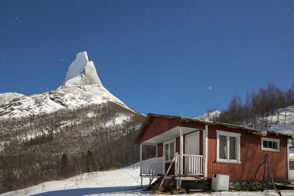 A typical house of fishermen called Rorbu frames the snowy Stetind mountain under the starry sky Tysfjord Nordland Norway Europe