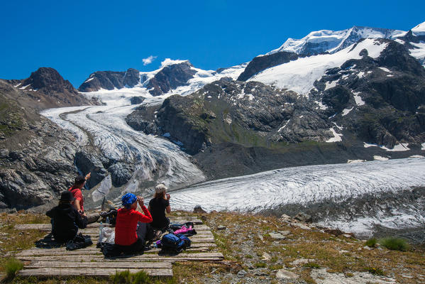 A group of hikers having a pic-nic right in front of the glacier of the Morteratsch and some snow-capped peaks of the Bernina Group, Engadine, Switerland Europe