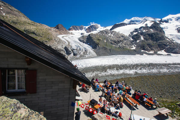 Hikers resting on the terrace of the Chamanna Boval Hut, enjoying the amazing view of the snow-capped peaks and perennial  glaciers of the Morteratsch valley - Engadine Switzerland Europe