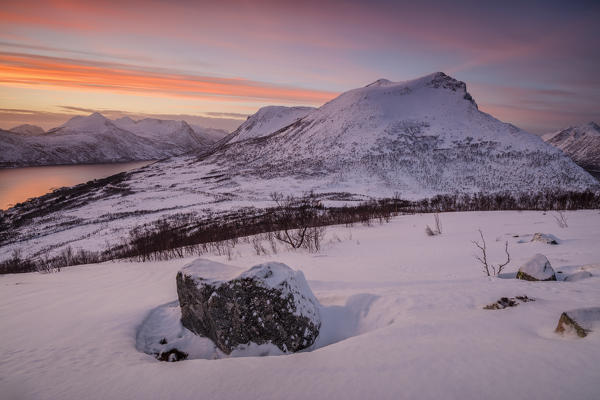 The frozen sea surrounded by snow framed by the orange sky at sunset Torsken Senja Troms County Norway Europe