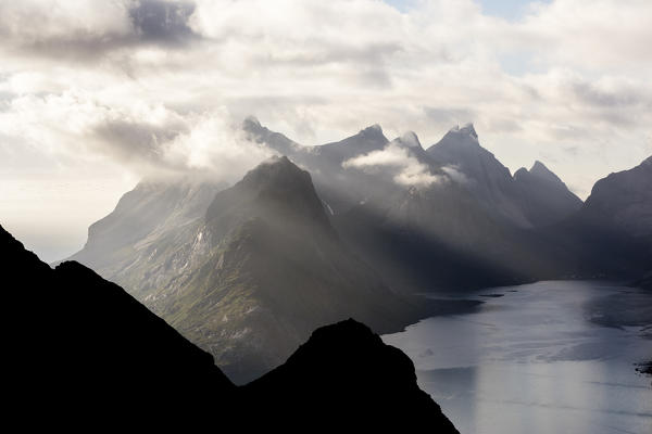 Top view of sea framed by silhouettes of peaks covered by clouds and mist Reinebringen Moskenes Lofoten Islands Norway Europe