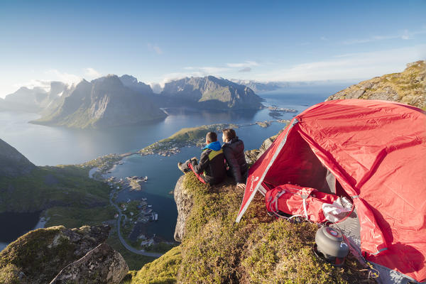 Hikers admire the blue sea framing the village from a tent on top of peak Reinebringen Moskenes Lofoten Islands Norway Europe