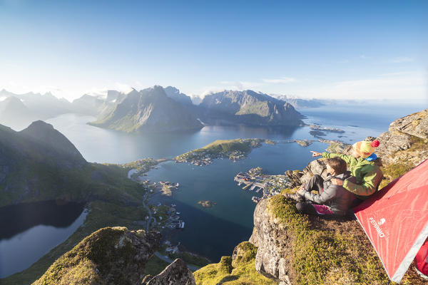 Hikers admire the blue sea framing the village from a tent on top of peak Reinebringen Moskenes Lofoten Islands Norway Europe