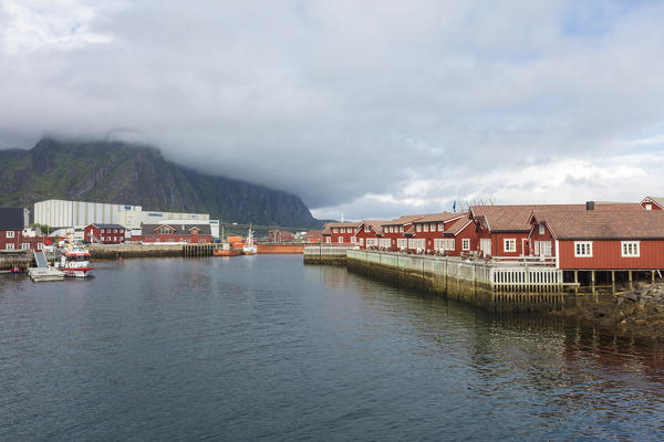 Clouds on rocky peaks frame the typical rorbu of fishing village surrounded by sea Svolvaer Vagan Lofoten Islands Norway Europe