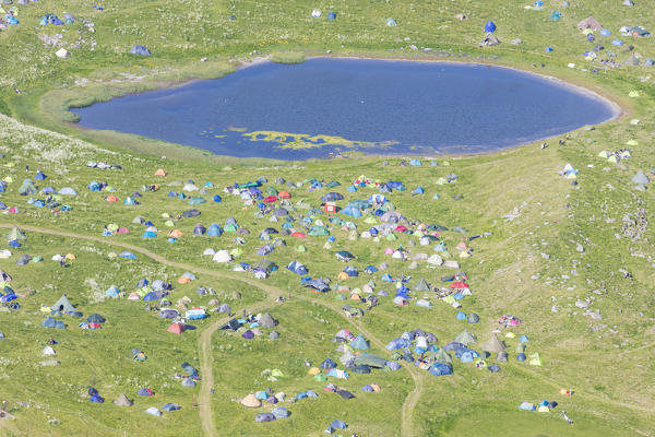 Campsite and tents in green meadows surrounded by a blue lake Vaeroy Island Nordland county Lofoten archipelago Norway Europe