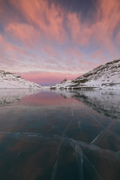 The frozen Lago Bianco framed by pink clouds at dawn Bernina Pass canton of Graubünden Engadine Switzerland Europe