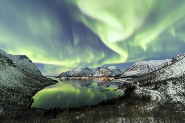 Northern lights and stars light up the snowy peaks reflected in the cold sea Bergsbotn Senja Tromsø Norway Europe