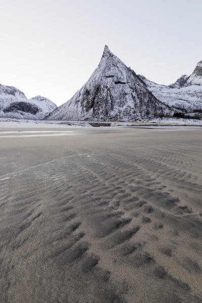 The sandy beach covered with ice frames the snowy peaks at dawn Ersfjord Senja Tromsø Norway Europe