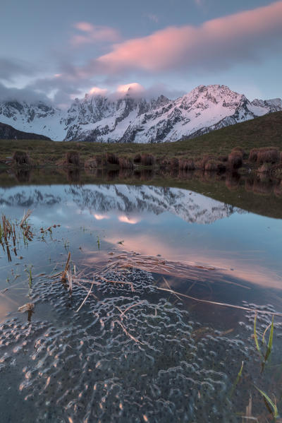 Snowy peaks and pink clouds reflected in water at dawn Tombal Soglio Bregaglia Valley canton of Graubünden Switzerland Europe