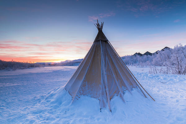 Pink sky at sunrise on isolated Sami tent in the snow, Abisko, Kiruna Municipality, Norrbotten County, Lapland, Sweden