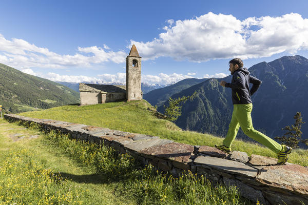 Hiker runs toward the old church, San Romerio Alp, Brusio, Canton of Graubünden, Poschiavo valley, Switzerland