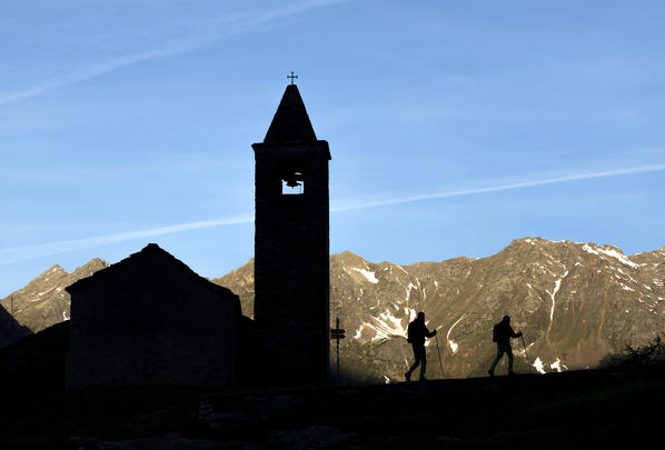 Silhouettes of hikers at the old church at dawn, San Romerio Alp, Brusio, Canton of Graubünden, Poschiavo valley, Switzerland