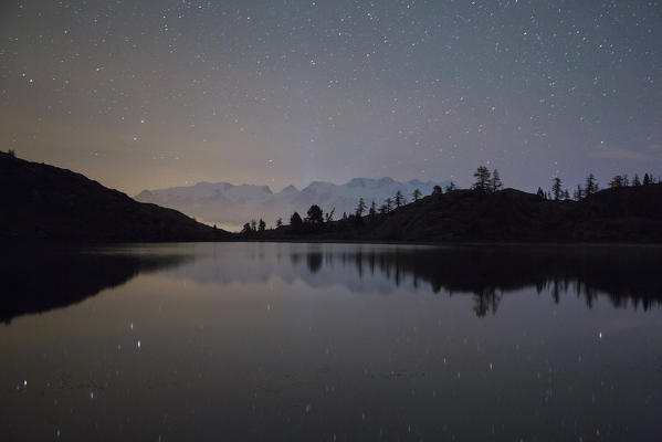 The group of Mount Rosa reflecting in Lake Bianco under a starry night Mont Avic natural park, Alps, Aosta valley, Italy Europe