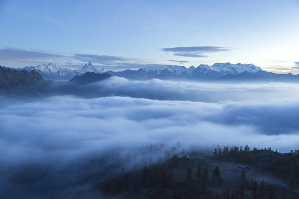 A soft veil of clouds cover the landscape of the Mount Avic natural park at dawn. In the background  the famous peaks of Matterhorn and Mount Rosa. Aosta Valley. Italy. Europe