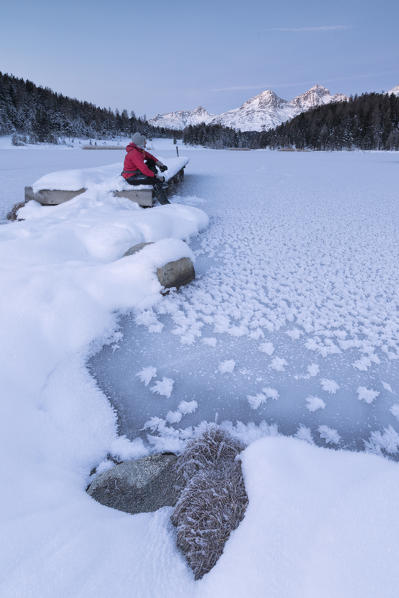 Man sitting on shore of frozen lake, Lej da Staz, St Moritz, canton of Graubünden, Engadine, Switzerland