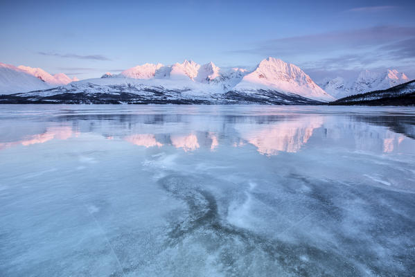 Snowy peaks are reflected in the frozen Lake Jaegervatnet at sunset Stortind Lyngen Alps Tromsø Lapland Norway Europe