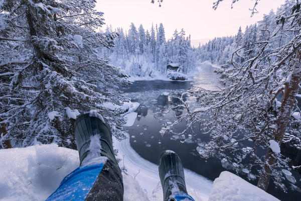 Hiker rests on the snow above Myllykoski rapids, Juuma, Oulanka National Park, Kuusamo, Lapland, Finland