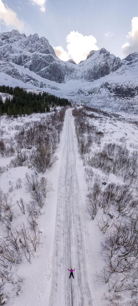 Panoramic aerial view of woman lying on the icy road to Nusfjord, Lofoten Islands, Norway