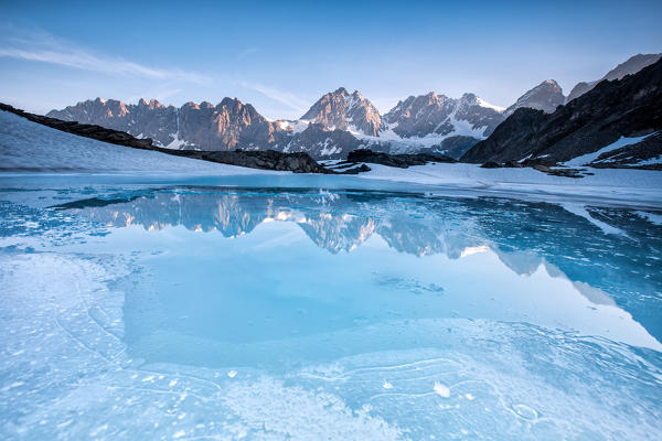 The reflection of the Bernina range in the icy water of little lake Forbici while melting - Alps, Valmalenco, Valtellina Sondrio, Lombardy, Italy Europe